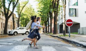 Side view of small school girls crossing street outdoors in town, running.