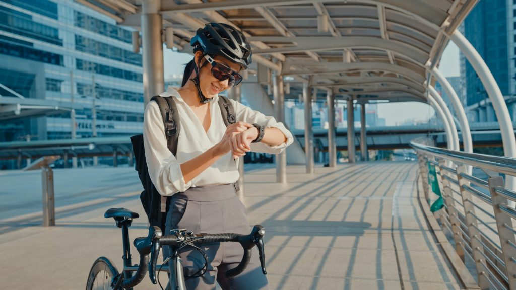 businesswoman with backpack bicycle smiling look smartwatch in city street go to work at office.