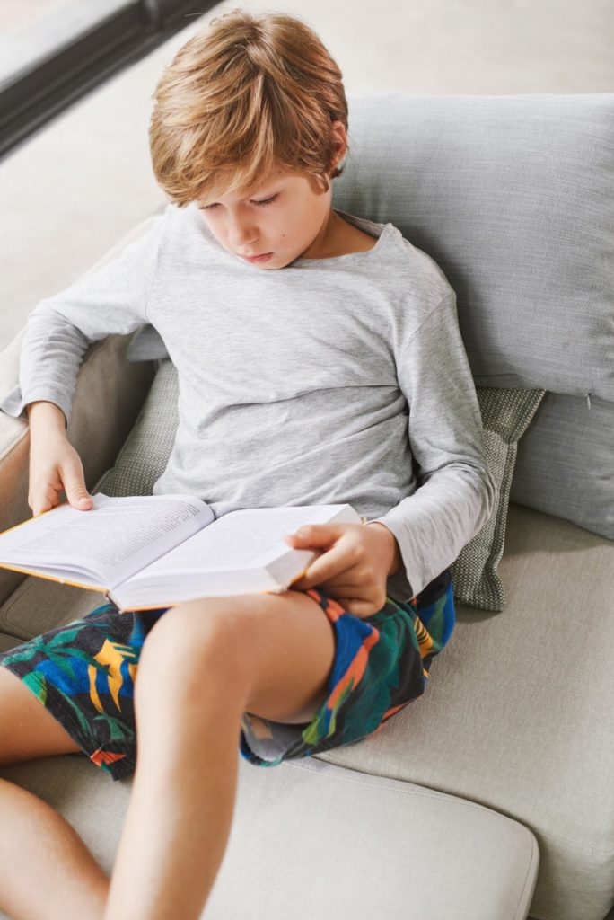 Boy is reading a book on a couch