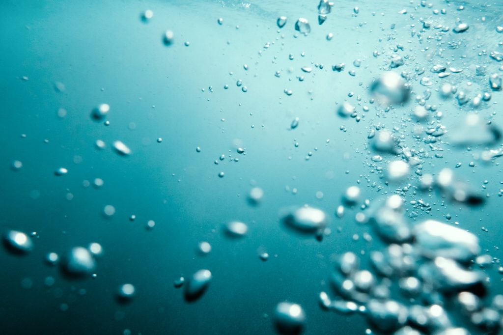 Underwater View of Bubbles In Deep Blue Ocean. Close Up Water. Background